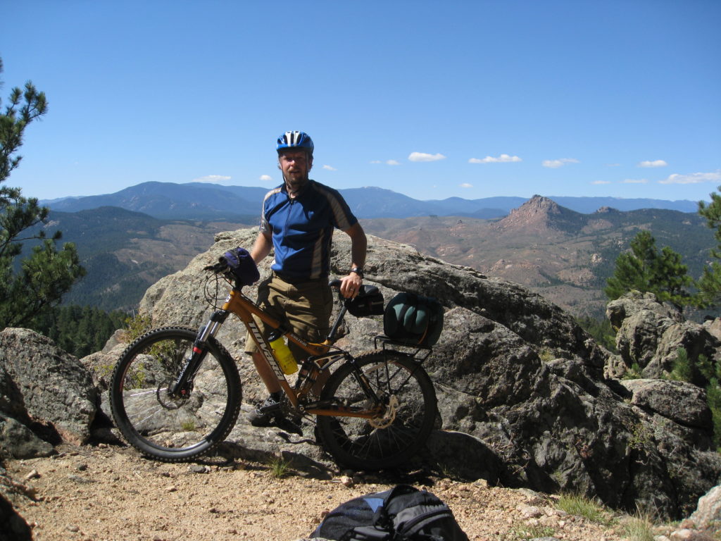 Nick standing with mountain bike near a rock looking tired