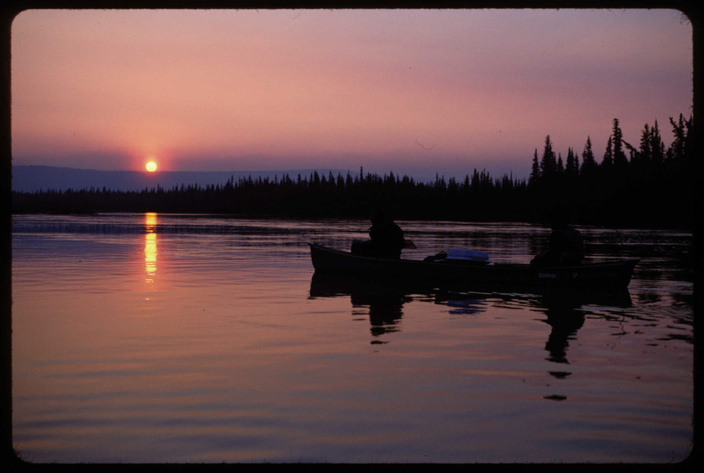 Canoe in a river at sunset with sun just touching horizon